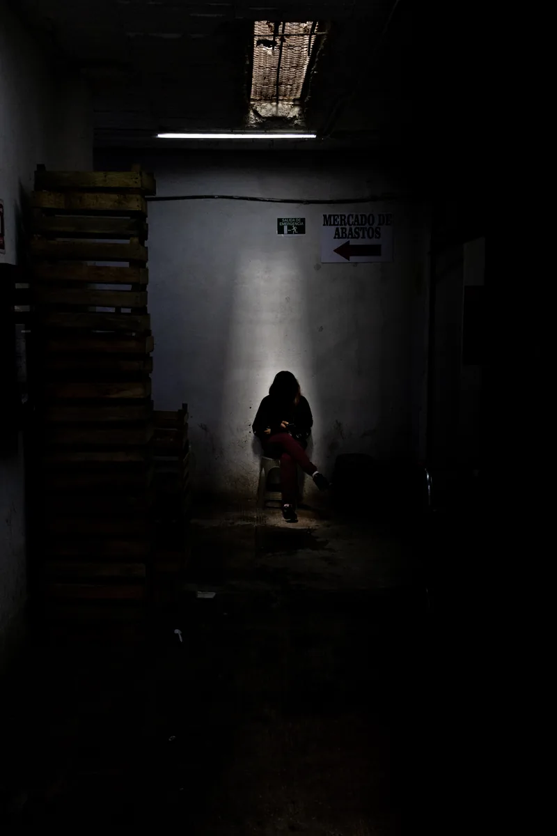 Una joven revisa su teléfono en un pasillo oscuro del mercado